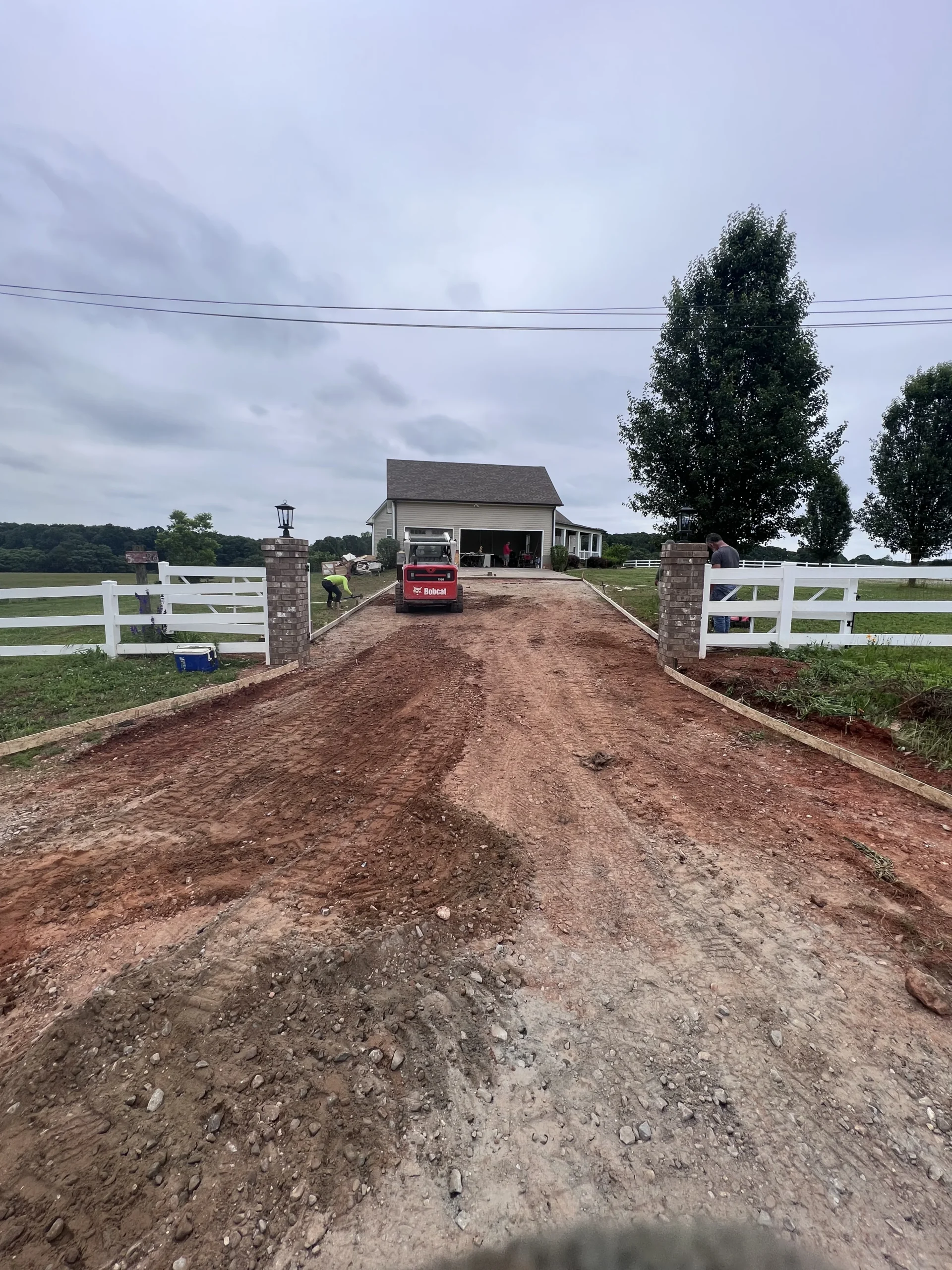 Excavator grading driveway base for new concrete installation