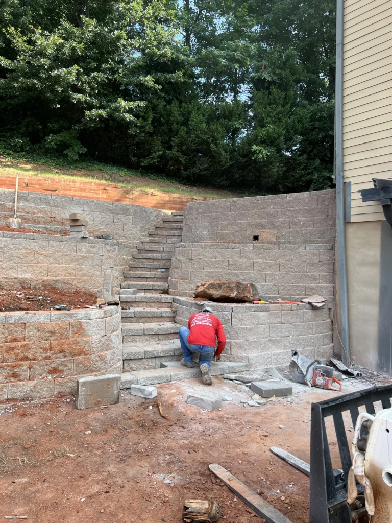 Mason installing custom block retaining wall and integrated stone steps for sloped backyard in Metro Atlanta